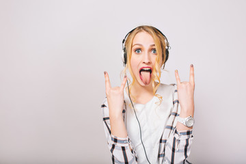 Fair-haired girl in white blouse shows tongue and fools around, listening hard rock music in big...