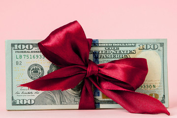 one hundred dollars gift wraped with a red ribbon on pink background