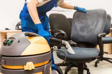 Obraz premium Young man in workwear and rubber gloves cleans the office chair with professional equipment.