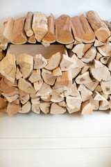 Neatly Stacked Split Firewood Indoors on Rack Against White Wall on Bright Maple Wooden Floor