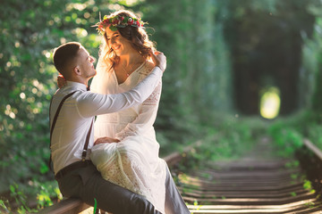 couple sitting and hugging on railway. tree tunnel. festive clot