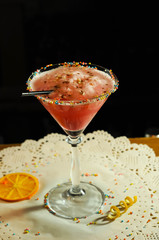 high stem glass with red alcohol drink and on white paper napkin with dried orange slice on table  in bar