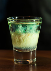 blue alcohol drink in clear shot glass on wooden counter in bar 