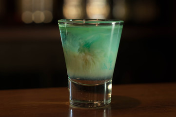 selective focus of shot glass with blue alcohol drink on wooden table in bar