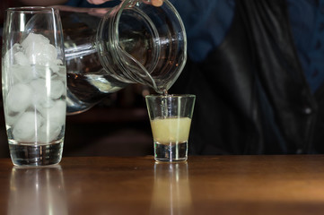 cropped view of barman at counter pouring soda from jug into glass with juice near glass with ice in bar 