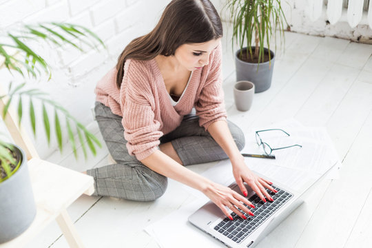 Young woman sits on the floor in a Scandinavian apartment interior with a laptop, studying law, freelance girl at work, distance learning student, online employment, paperwork and outsourcing concept