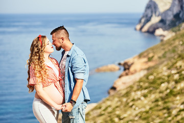 Young pregnant woman walking with her husband against sea background