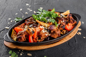 Baked meat with grilled vegetables, greens and almond in pan on black stone background. Hot Meat Dishes