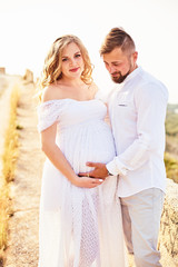 Obraz premium Portrait of a young pregnant woman posing with her husband on a sunny summer day