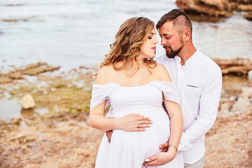 Portrait of a young pregnant woman posing with her husband on the beach