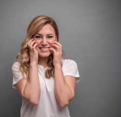 A young woman holds her forehead with her hands and screams. On a gray background.