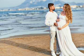 Fototapeta na wymiar Young pregnant woman posing with her husband on the beach