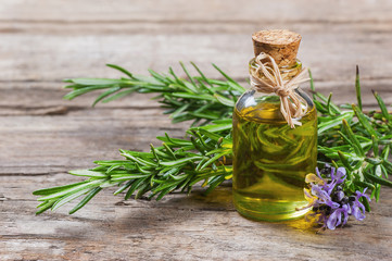 Top view Bottle glass of essential rosemary oil with rosemary branch and flower on wooden rustic...