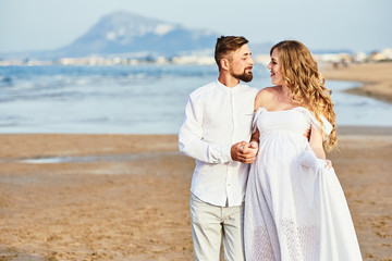 Young pregnant woman posing with her husband on the beach