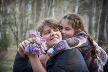 In the spring in the forest, a little girl hugs her mother and gives her a bouquet of flowers.