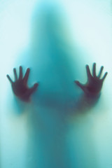 Blurred shadow of a horror woman. The hands on the glass. Dangerous person behind frosted glass. Person of mystery Halloween background. Fear, terror, mystery