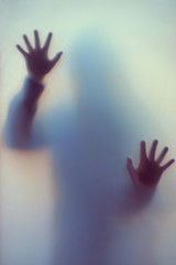 Blurred shadow of a horror woman. The hands on the glass. Dangerous person behind frosted glass. Person of mystery Halloween background. Fear, terror, mystery