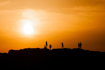 Black silhouettes of people standing on the top of a peak and watching sunset, sunrise. Mountain sunset, sunrise.