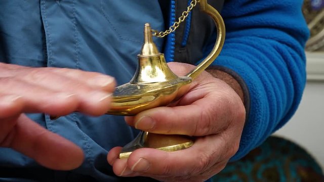 Handheld, close up, interior shot of a hand rubbing a gold lamp.