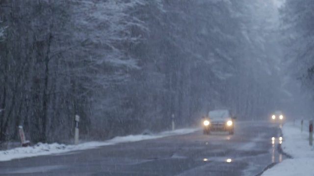 Car driving along the forest road in winter. Snowing.