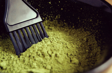 Macro of green natural henna powder in a bowl with black brush. Organic care and eco dye for hair. Dried lawsonia inermis as colorant.
