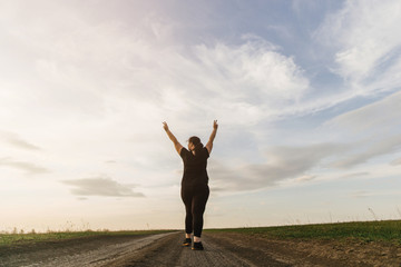 Body positive, freedom, high self esteem, confidence, happiness, inspiration, success, positive affirmation. Overweight woman celebrating rising hands to the sky on summer meadow.