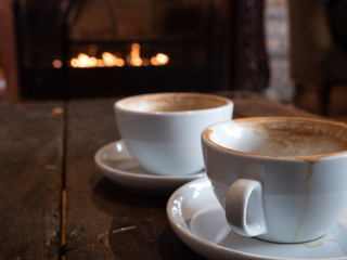 Two cups of Coffee with fireplace in background