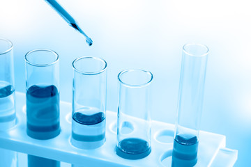 Close up, scientist dropping blue liquid into test tubes,   concept of laboratory equipment in science experiments.