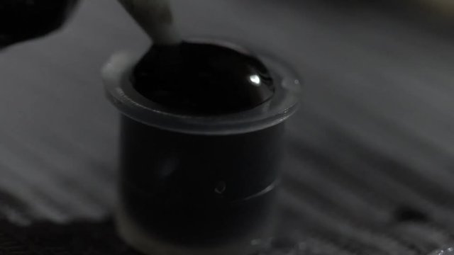 Close-up shot of a tattoo artist mixing black ink in ink cap