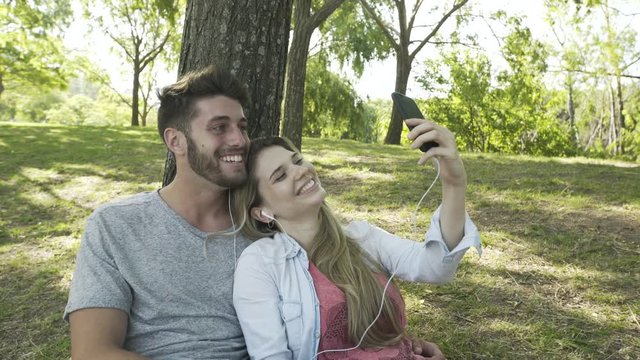 Medium shot of smiling young couple listening to music and taking selfie with a smartphone