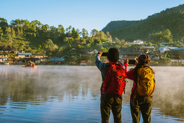 An Asian couple who is standing and watching the fog rising on the lake in the morning. Travel Ban Rak Thai village, Mae Hong Son in Thailand. Take a picture of the lake