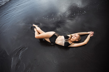 The girl in the swimsuit, lying on the black sand.