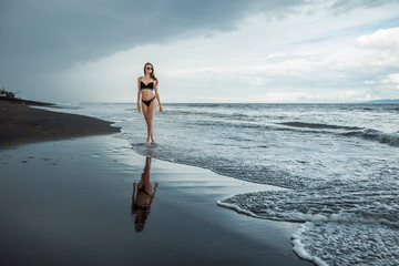 Thin girl in a swimsuit goes on the black beach.
