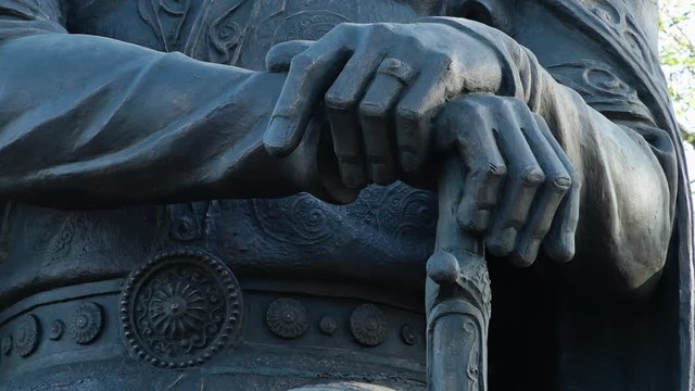 Steady, extreme close up shot of a statue of hands resting on top of a sword.