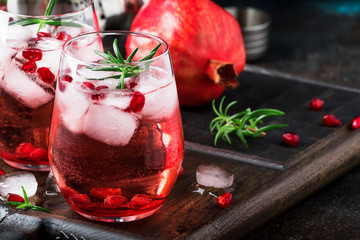 Red cocktail with cold vodka and pomegranate juice, ice cubes and rosemary, bar tools, blue black bar counter background, copy space, selective focus