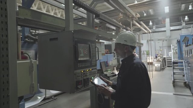 Medium shot of engineer using digital tablet and examining machinery in factory