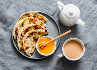 Indian paratha flatbread with honey and masala tea on grey background, top view