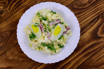 Salad with chinese cabbage, onion, sausage, eggs and mayonnaise on wooden table