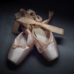 Pointe shoes ballet dance shoes with a bow of ribbons beautifully folded on a dark background.