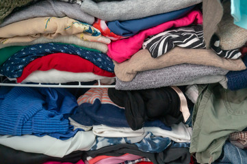 Messy folded clothes crammed in a closet on a shelf. Depicting woman's wardrobe, consumerism,...