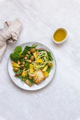 Vegetarian salad with pineapple, olives, tofu, zucchini, spinach and chickpeas in rustic plate on marble background with copy space