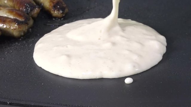 Pouring pancake batter on a hot grill next to link sausage