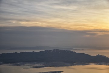 Fototapeta premium Aerial view from airplane of Antelope Island at sunset, view from Magna, sweeping cloudscape at sunrise with the Great Salt Lake State Park in winter. USA, Utah.