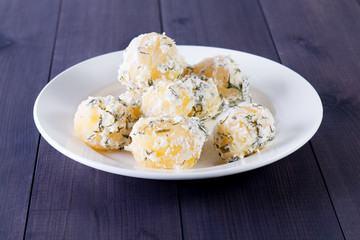 Boiled young potatoes with sour cream and dill on a wooden background