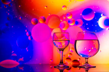 transparent glasses with water and oily drops on colorful background 