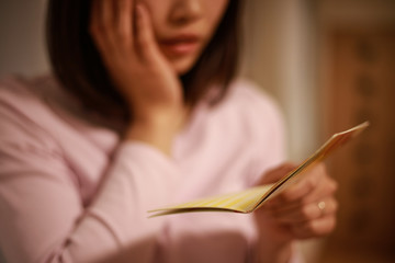 貯金通帳を見て悩む女性