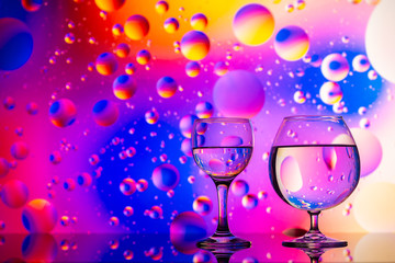 transparent glasses with water and oily drops on colorful background 