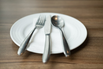 White plate and cutlery  on wooden table