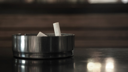 Closeup of cigarette inside an ashtray on top of a black table with slightly orange light reflection from the restaurant. Selected focus.