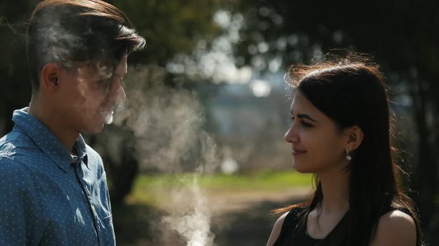 Vaping people talking outdoors. Young couple standing in the park.